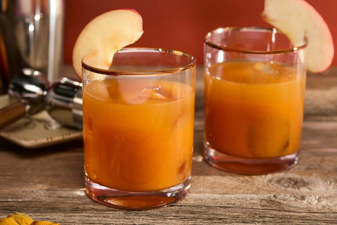 pumpkin colored drink in old fashioned glasses with apple slice garnish